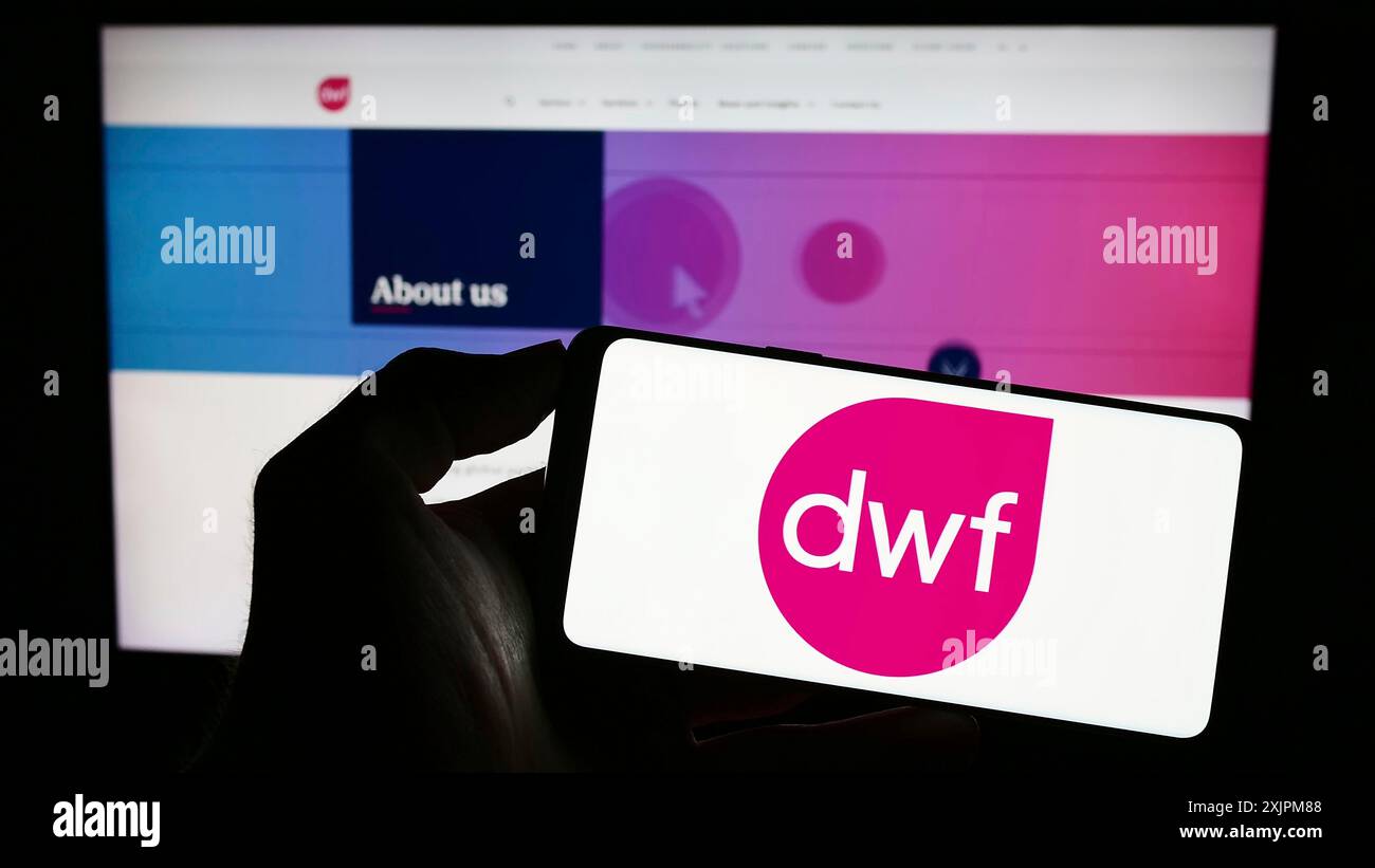 Stoccarda, Germania, 07-22-2023: Persona che detiene un telefono cellulare con il logo della società legale britannica DWF Group plc sullo schermo di fronte alla pagina web aziendale. Foto Stock