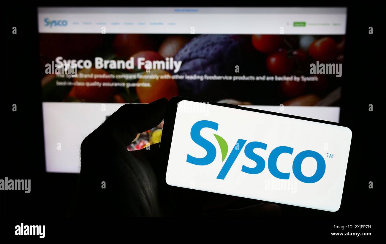 Stoccarda, Germania, 08-09-2023: Persona che detiene il cellulare con il logo della società all'ingrosso statunitense Sysco Corporation sullo schermo di fronte alla pagina web aziendale. Foto Stock