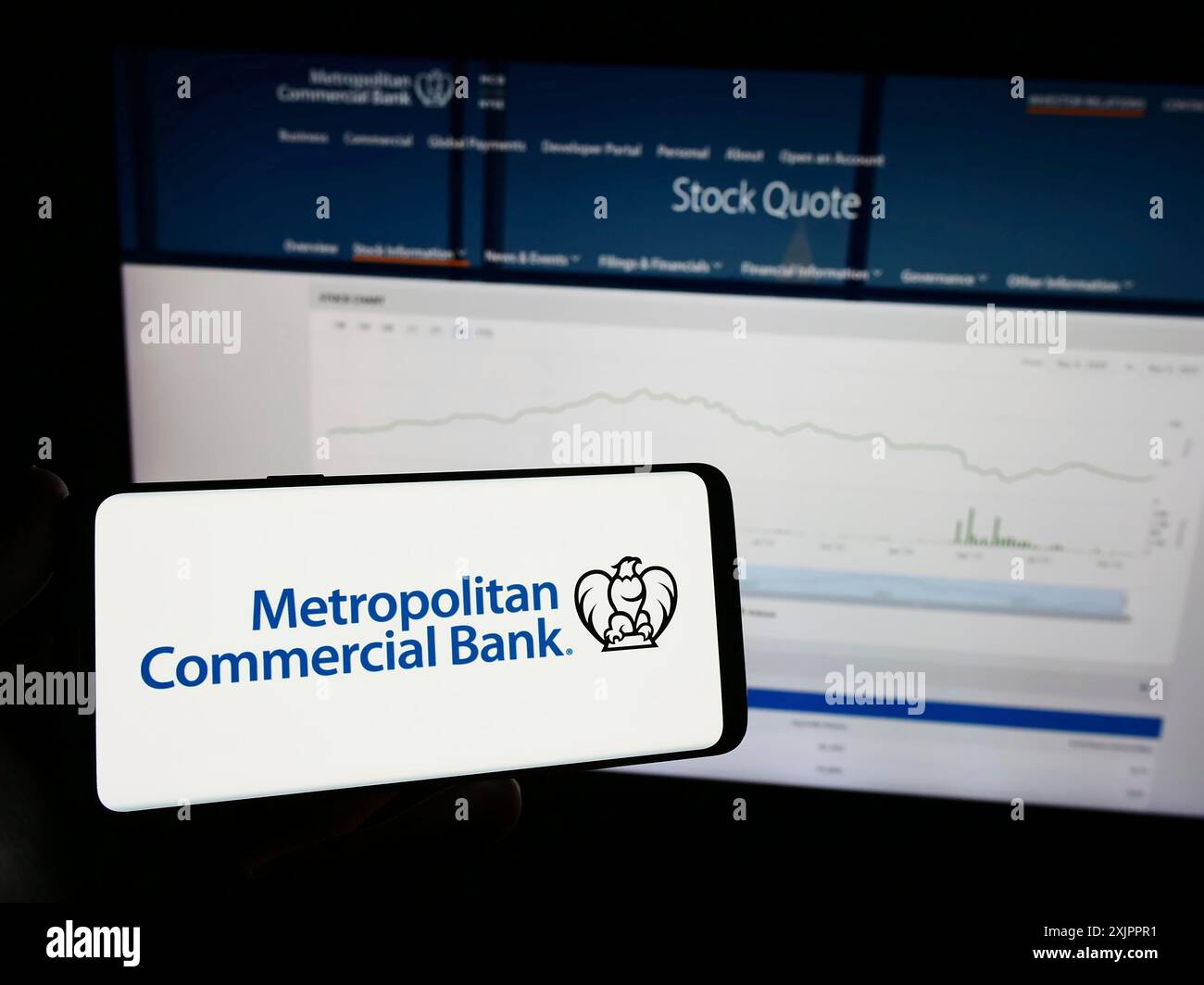 Stoccarda, Germania, 11-07-2023: Persona che detiene un telefono cellulare con il logo della società finanziaria statunitense Metropolitan Commercial Bank (MCB) davanti al web Foto Stock