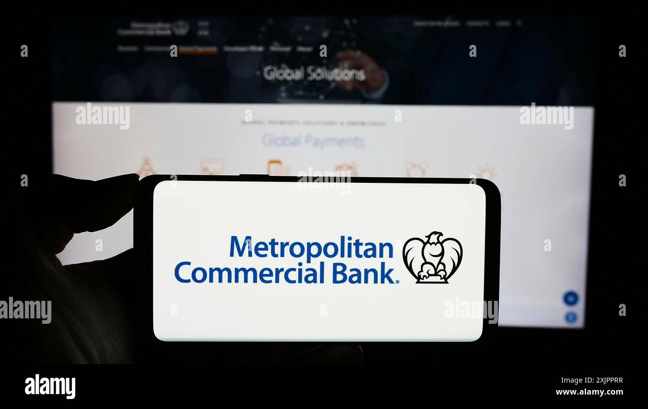 Stoccarda, Germania, 11-07-2023: Persona che detiene il cellulare con il logo della società finanziaria statunitense Metropolitan Commercial Bank (MCB) davanti alla pagina web. Foto Stock