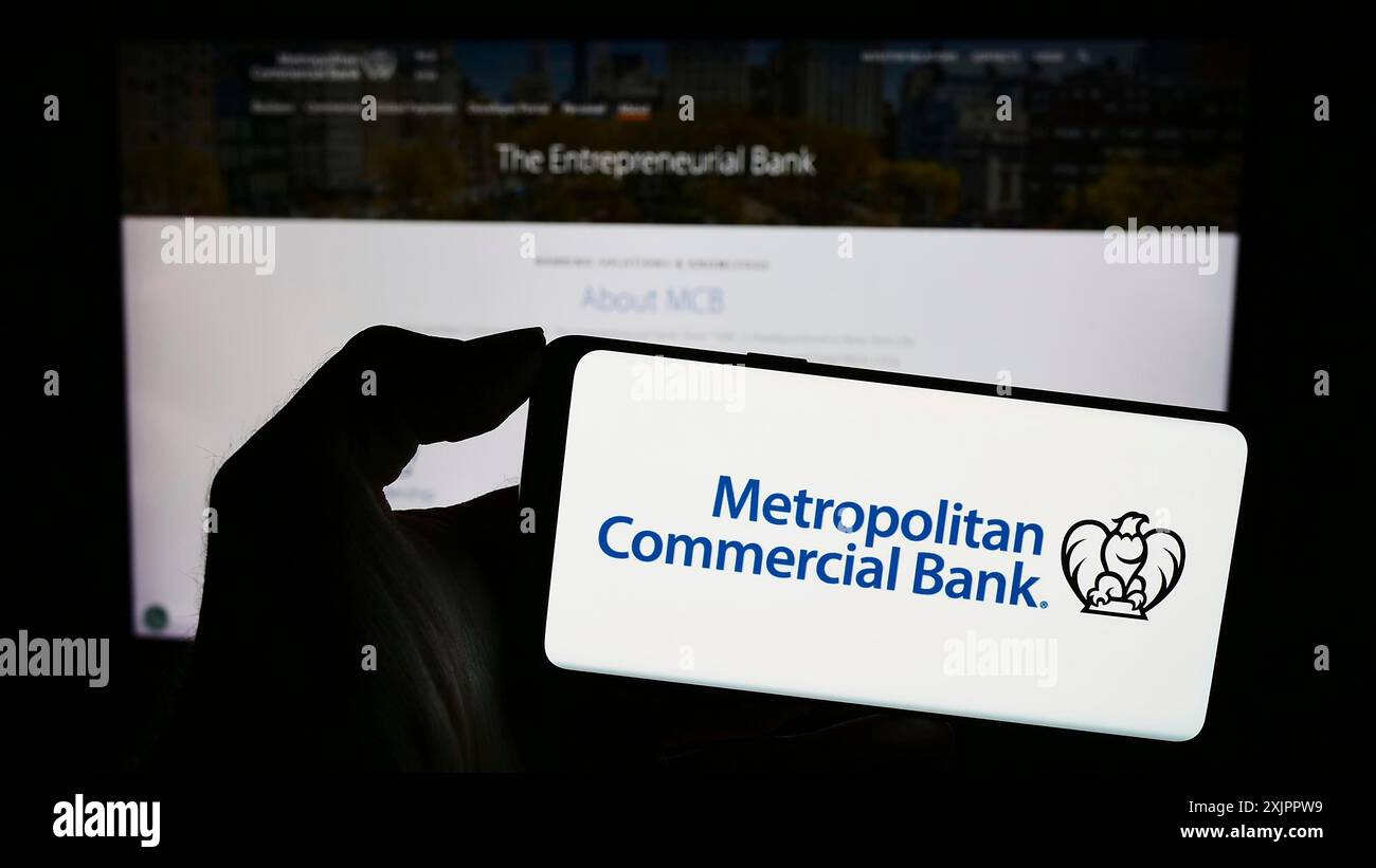 Stoccarda, Germania, 11-07-2023: Persona con smartphone con logo della società finanziaria statunitense Metropolitan Commercial Bank (MCB) davanti al sito web. Foto Stock