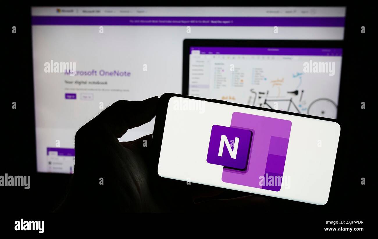 Stoccarda, Germania, 09-21-2023: Persona che tiene un telefono cellulare con logo del software per appunti Microsoft OneNote sullo schermo davanti al Web aziendale Foto Stock