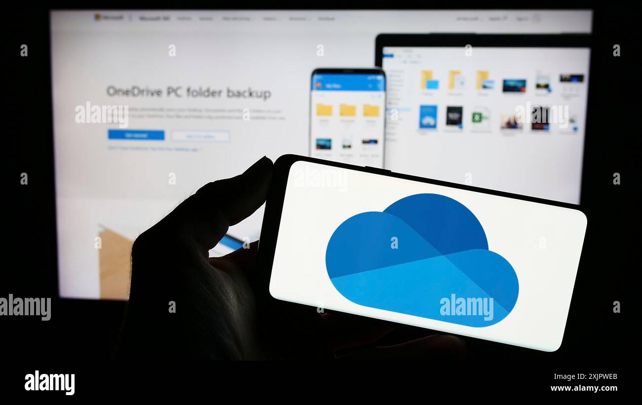 Stoccarda, Germania, 09-21-2023: Persona che detiene un telefono cellulare con il logo del servizio di hosting di file Microsoft OneDrive sullo schermo di fronte al sito web dell'azienda Foto Stock
