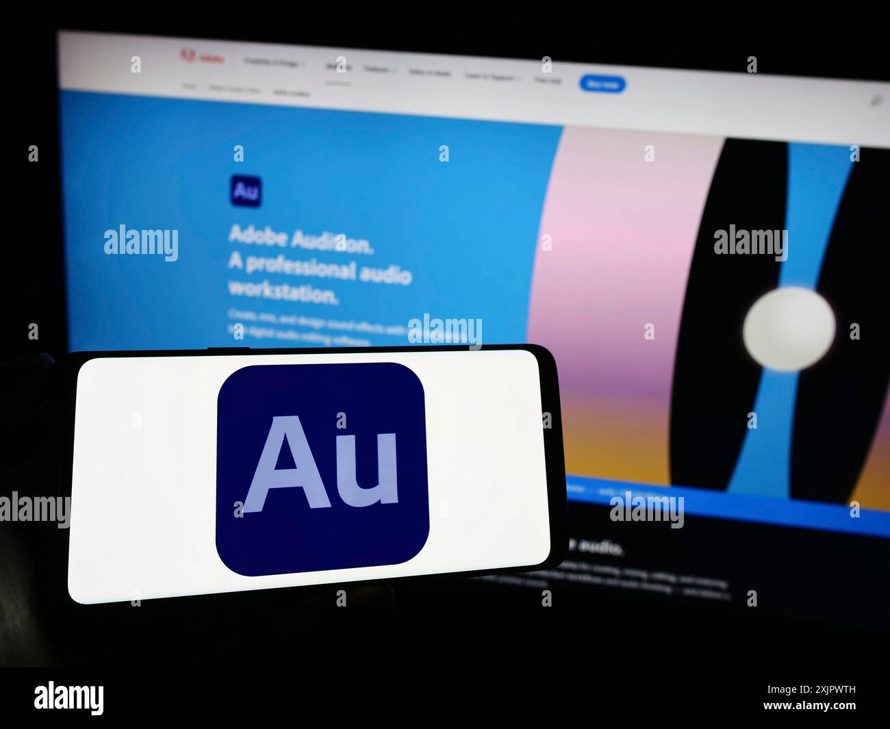 Stoccarda, Germania, 09-23-2023: Persona che tiene un telefono cellulare con il logo della workstation audio digitale Adobe Audition sullo schermo di fronte al Web aziendale Foto Stock