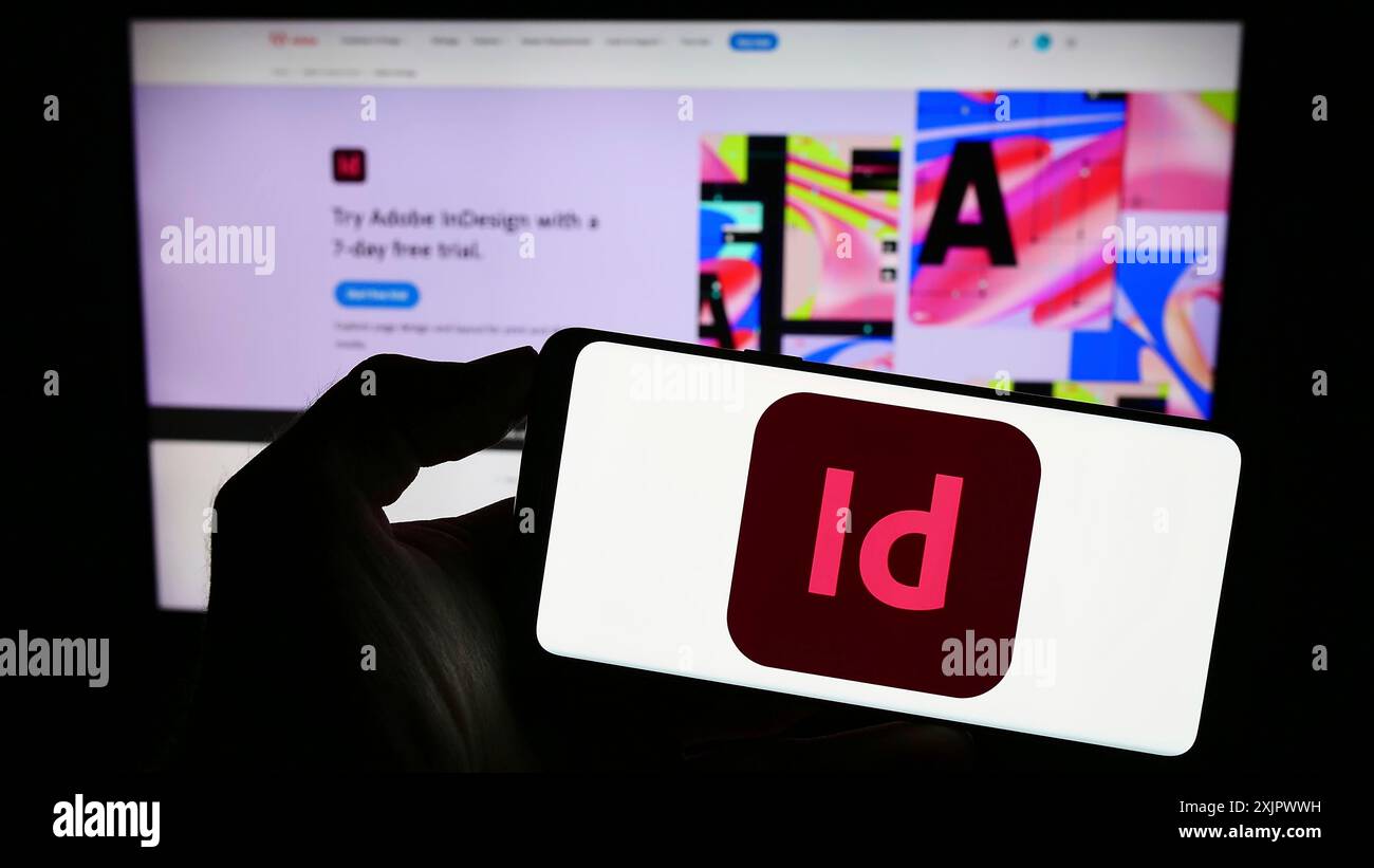Stoccarda, Germania, 09-23-2023: Persona che detiene un telefono cellulare con il logo del software di desktop publishing Adobe InDesign sullo schermo davanti alla pagina Web. Foto Stock