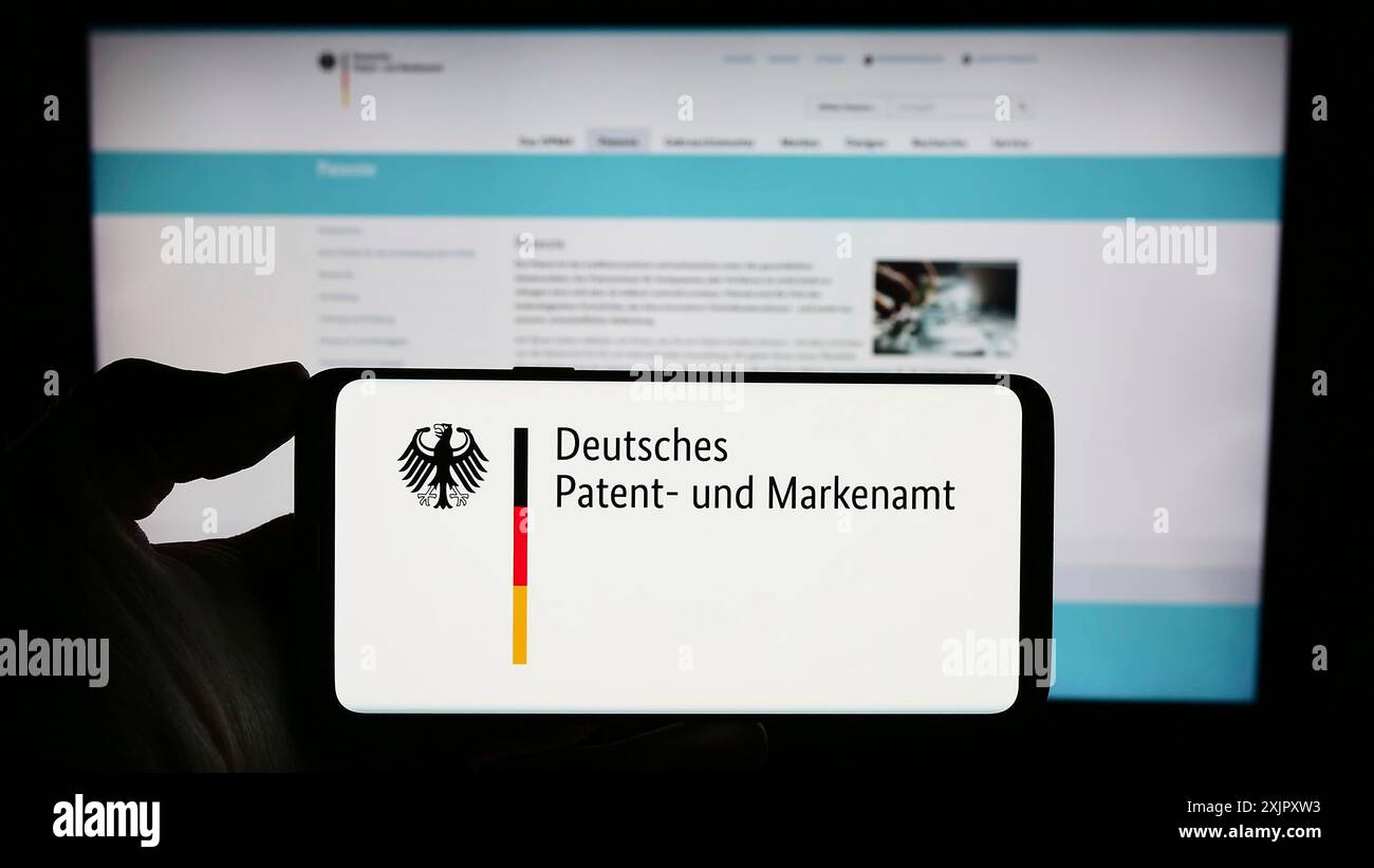 Stoccarda, Germania, 10-17-2023: Persona che detiene il cellulare con il logo dell'agenzia tedesca Deutsches Patent- und Markenamt (DPMA) davanti alla pagina web. Concentrati Foto Stock