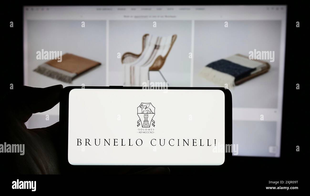 Stoccarda, Germania, 11-07-2023: Persona che detiene un cellulare con il logo dell'azienda italiana di moda Brunello Cucinelli Spa davanti al business web Foto Stock