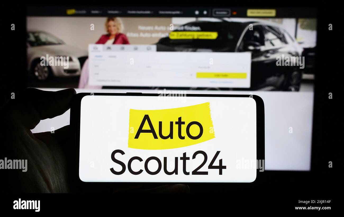 Stoccarda, Germania, 11-14-2023: Persona che detiene un telefono cellulare con il logo della società tedesca AutoScout24 GmbH sul mercato online di automobili, davanti alla pagina web. Foto Stock