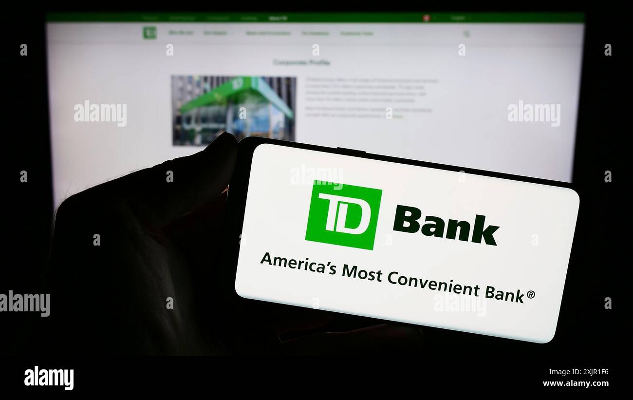 Stoccarda, Germania, 11-21-2023: Persona che detiene il cellulare con il logo della società di servizi finanziari Toronto-Dominion Bank (TD) davanti all'azienda Foto Stock