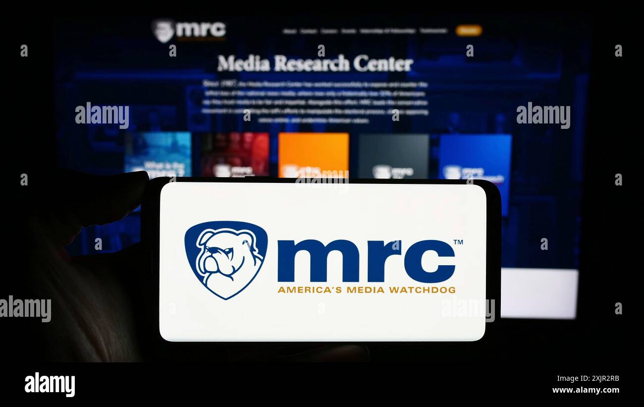 Stoccarda, Germania, 12-14-2023: Persona che tiene il cellulare con il logo dell'organizzazione di controllo Media Research Center (MRC) davanti alla pagina web. Concentrati su Foto Stock