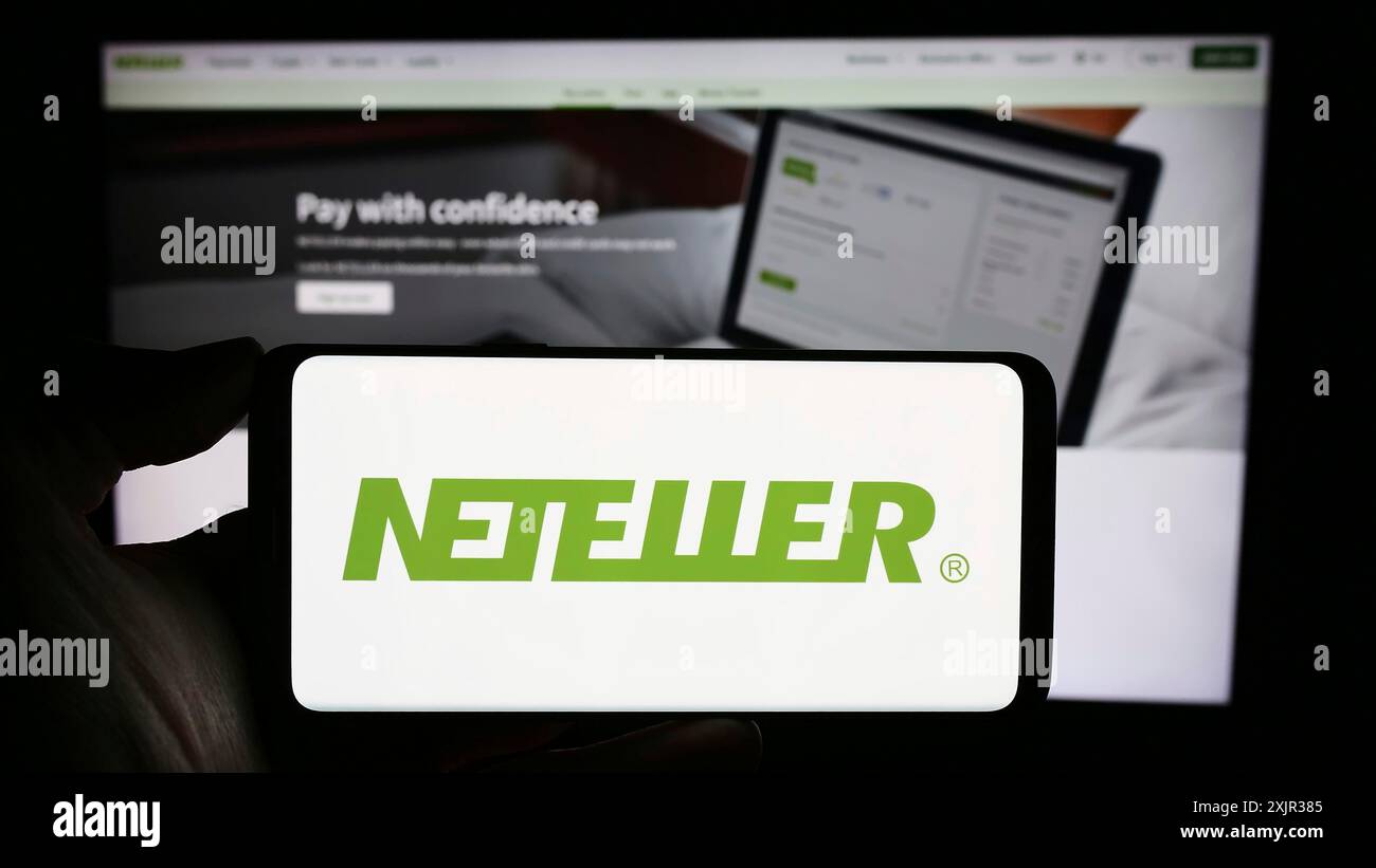 Stoccarda, Germania, 12-18-2023: Persona che detiene un cellulare con il logo della società di piattaforme di pagamento globale Neteller davanti alla pagina web aziendale. Concentrati Foto Stock