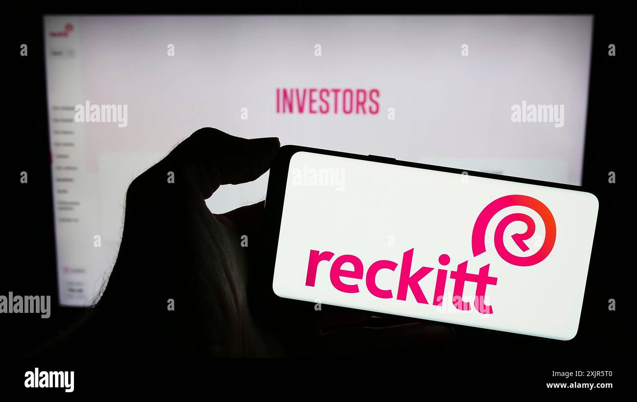 Stoccarda, Germania, 11-21-2023: Persona che detiene un telefono cellulare con il logo della società di beni di consumo Reckitt Benckiser Group plc di fronte al business web p Foto Stock