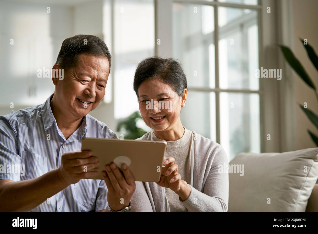 felice coppia asiatica anziana seduta sul divano a casa usando un tablet digitale insieme Foto Stock