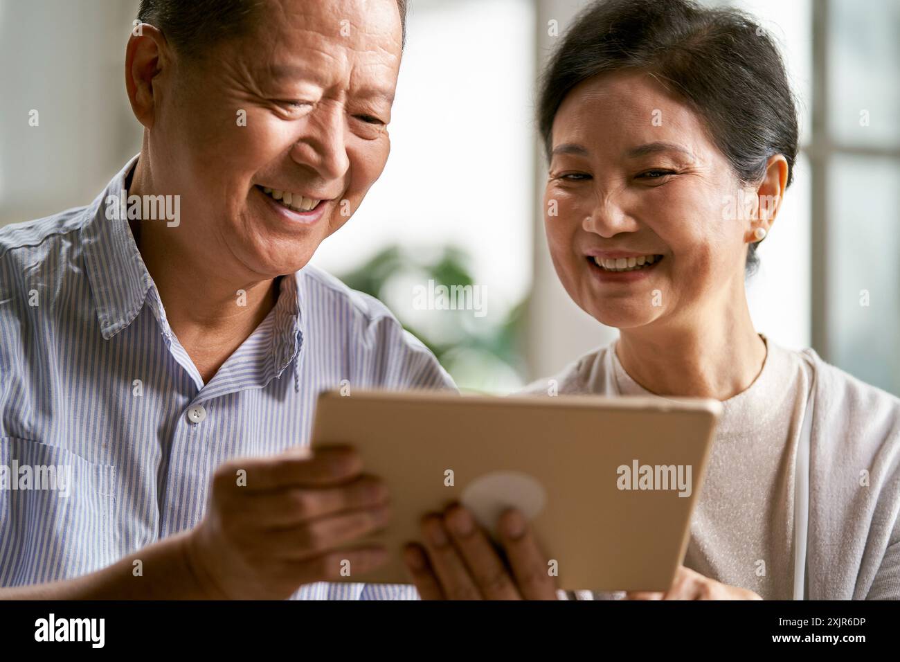 felice coppia asiatica anziana seduta sul divano a casa usando un tablet digitale insieme Foto Stock