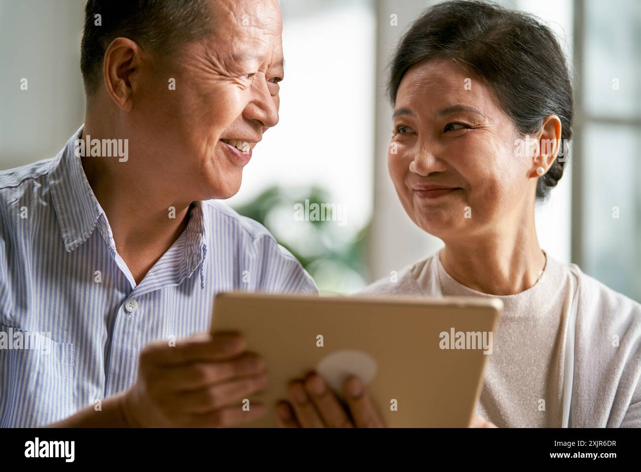 felice coppia asiatica anziana seduta sul divano a casa usando un tablet digitale insieme Foto Stock