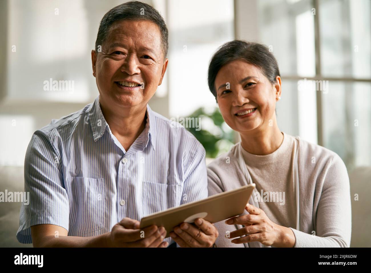 felice coppia asiatica anziana seduta sul divano a casa usando un tablet digitale insieme Foto Stock