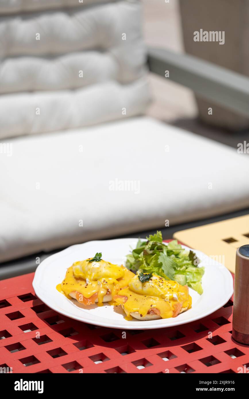 Un delizioso piatto di uova Benedict condite con ricca salsa hollandaise, accompagnato da un contorno di insalata fresca. Il piatto è presentato splendidamente Foto Stock