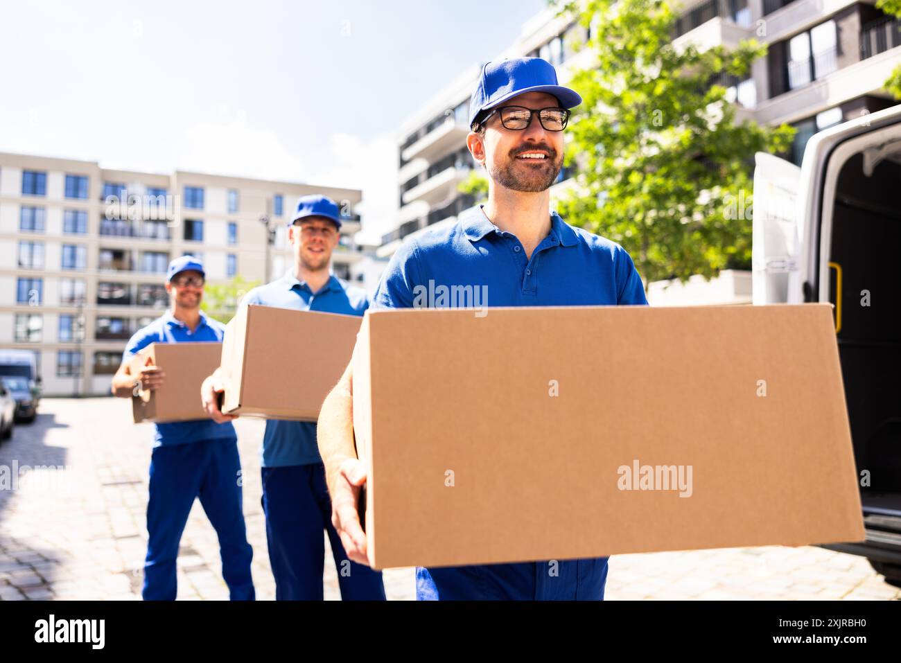 Uomini che lavorano sodo trasportano scatole di cartone in furgone - corrieri efficienti per il servizio logistico della catena di fornitura aziendale locale. Foto Stock