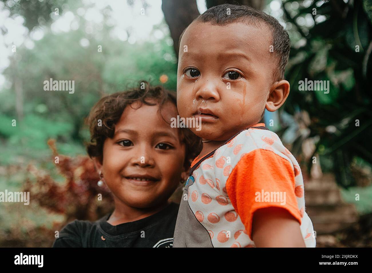 Ritratto espressivo di bambini balinesi: Una ragazza tiene un ragazzo pianto tra le braccia a Bali, Indonesia, 9 gennaio 2015 Foto Stock