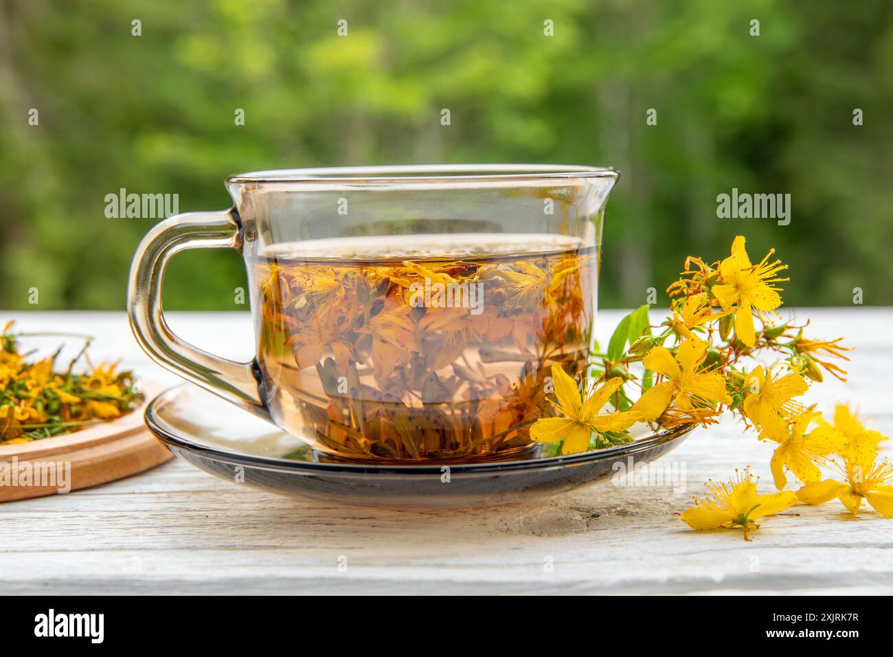 Hypericum perforatum comunemente noto come erba di San Giovanni, perfora erba di San Giovanni o tè a base di erbe di erba di San Giovanni comune in vetro su una tavola di legno bianca. Foto Stock
