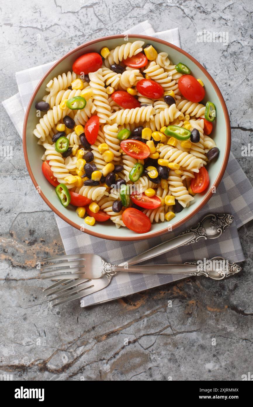Insalata di pasta fusilli fresca, fagioli neri, pomodori e mais in un piatto sul tavolo. Vista dall'alto verticale Foto Stock
