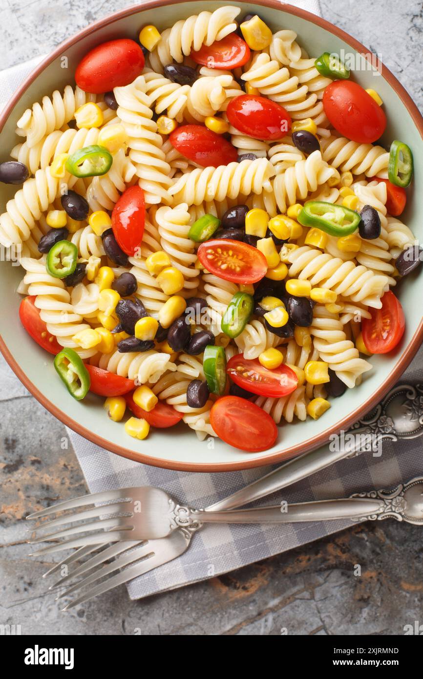 Mescolare l'insalata di pasta con fagioli neri, pomodoro, jalapeno e mais in un piatto sul tavolo. Vista dall'alto verticale Foto Stock