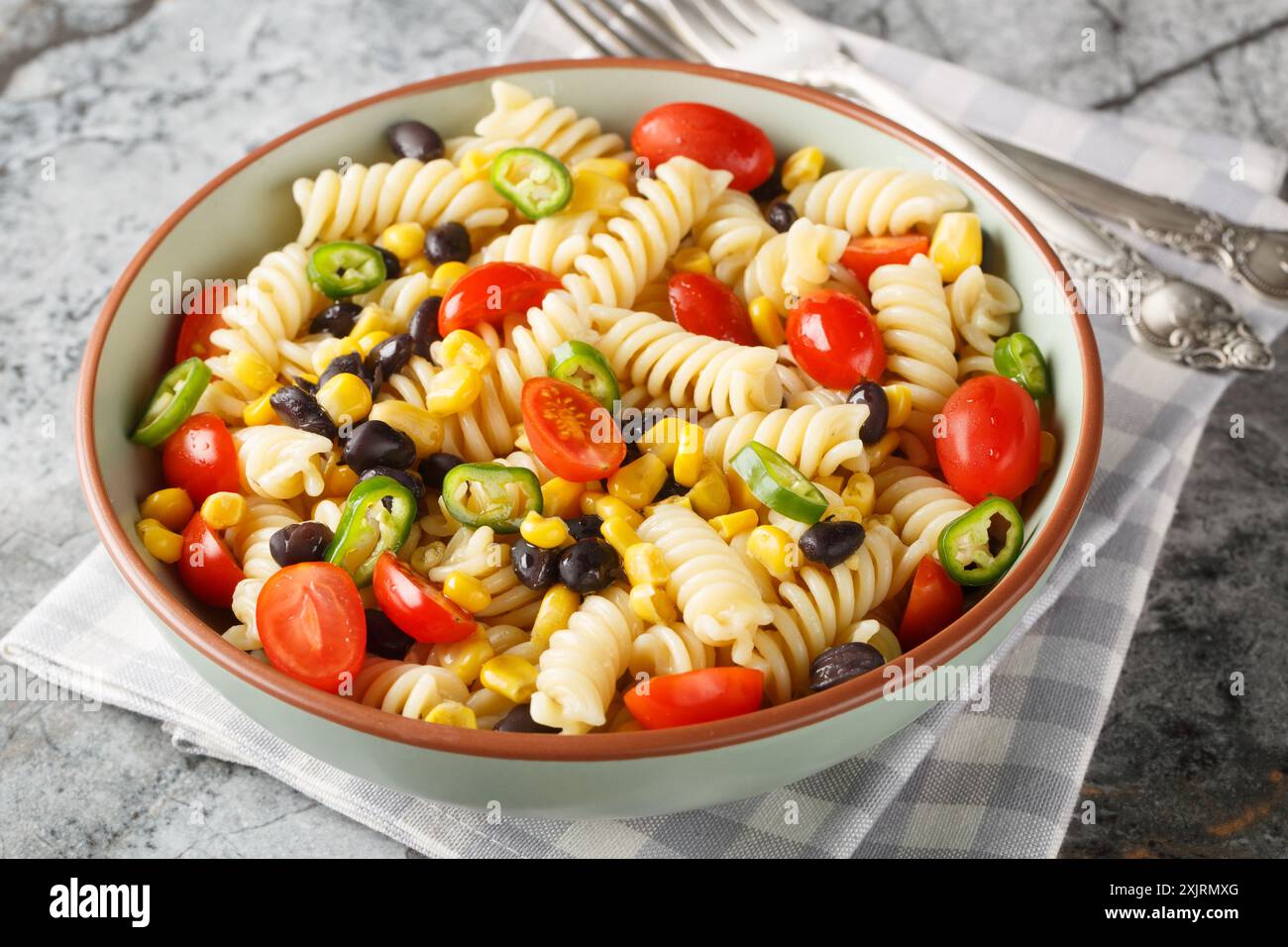 Fusilli con fagioli neri, pomodoro, jalapeno e mais in primo piano in un piatto sul tavolo. Orizzontale Foto Stock