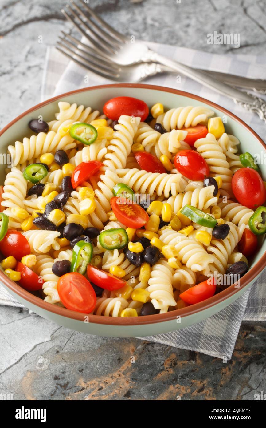 Insalata di pasta fusilli fresca, fagioli neri, pomodori e mais in un piatto sul tavolo. Verticale Foto Stock