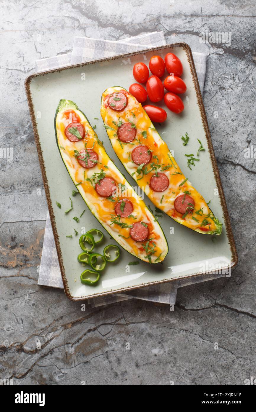 Metà di zucchine cotte con cheddar e mozzarella, salsicce e salsa di pomodoro da vicino in un piatto sul tavolo. Vista dall'alto verticale Foto Stock