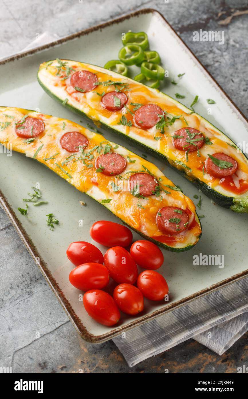 Pizza Boats con zucchine a basso contenuto di carboidrati cotti con cheddar e mozzarella, salsicce e salsa di pomodoro da vicino in un piatto sul tavolo. Verticale Foto Stock