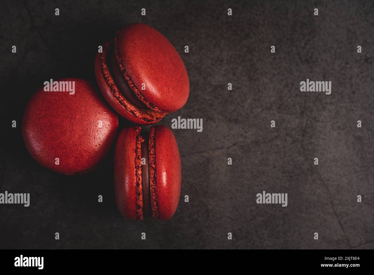 Tre macaron rossi, ciascuno con ripieno di cioccolato, sono disposti su uno sfondo di ardesia scura. I macaron sono posizionati in una forma triangolare, con TH Foto Stock