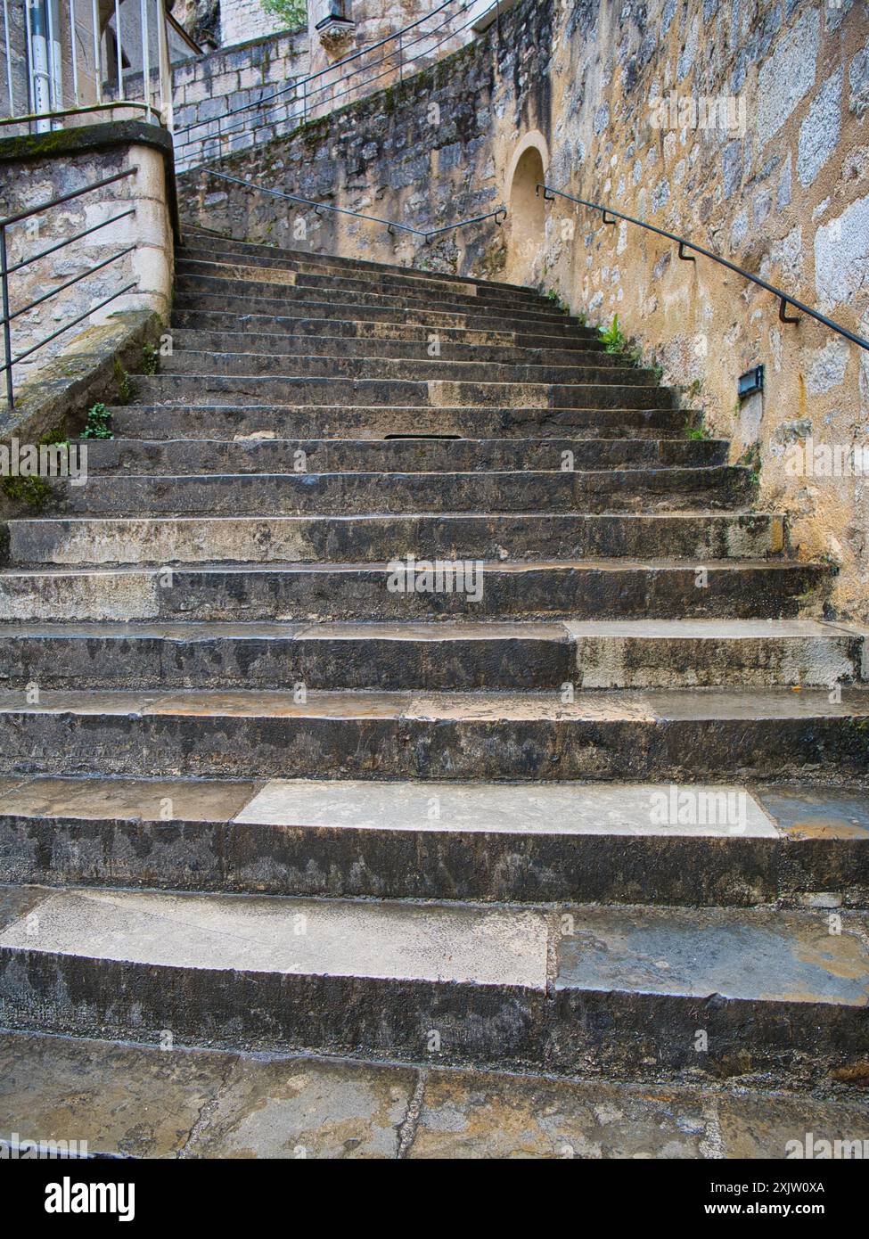 Guarda su una ripida rampa di gradini in pietra bagnati, grigi e all'aperto con un corrimano in metallo nero sulla destra. Preso a Rocamadour, nella regione Dordogna di p. Foto Stock