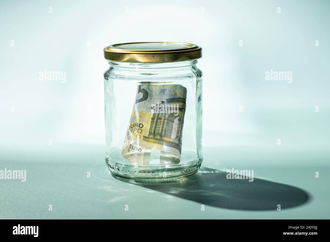 Banconota da cinque euro in un bicchiere con sfondo turchese e ombra dura Foto Stock