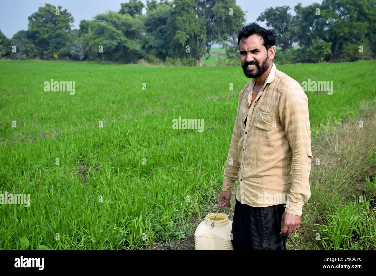 Un uomo contadino in piedi nel campo verde con un contenitore d'acqua Foto Stock