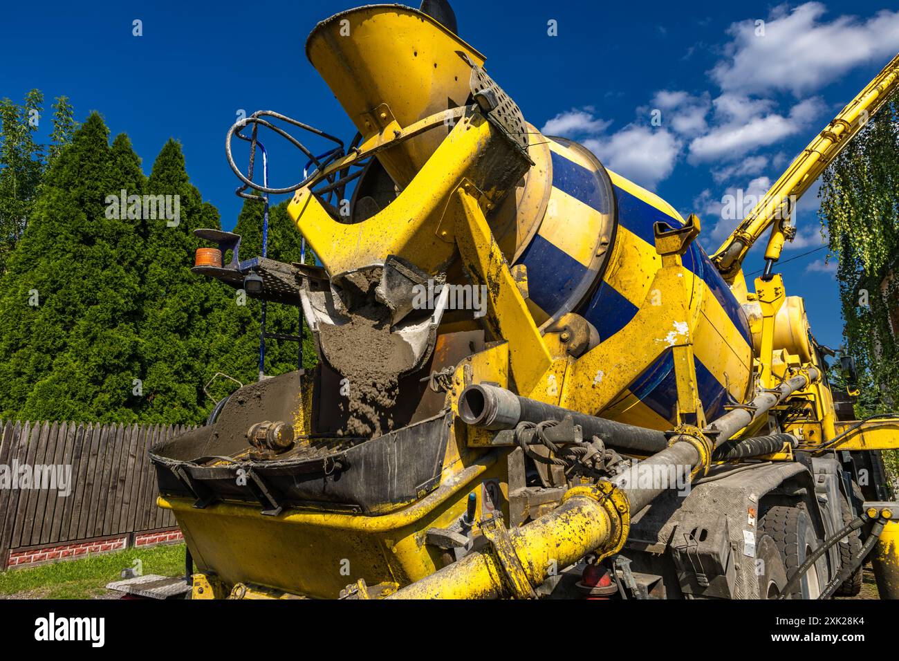 Una grande betoniera nera e gialla mescola e versa cemento mentre costruisce le fondamenta di una casa Foto Stock