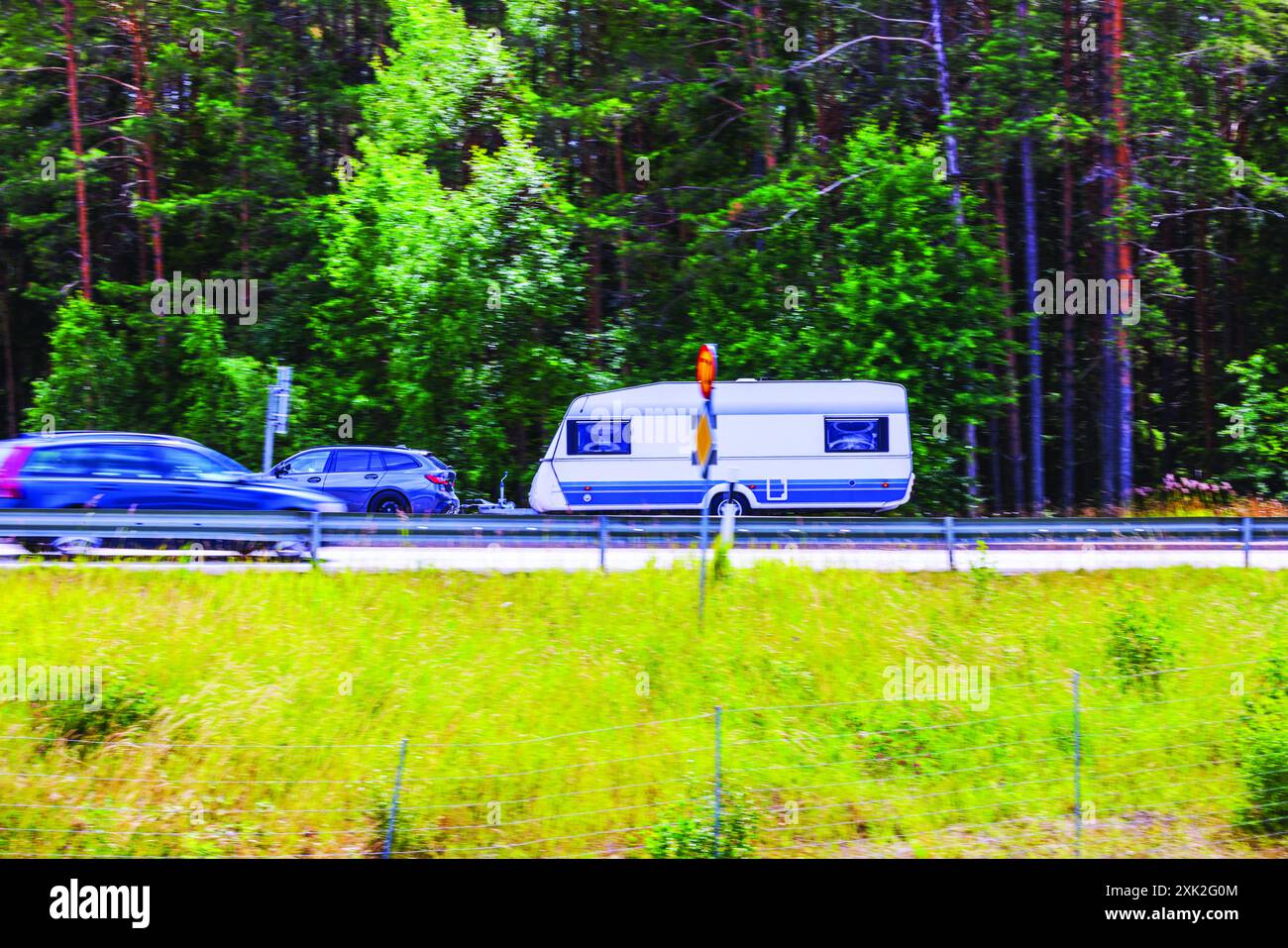 Splendido paesaggio estivo con traffico in movimento e un'auto che traina un rimorchio a casa. Foto Stock