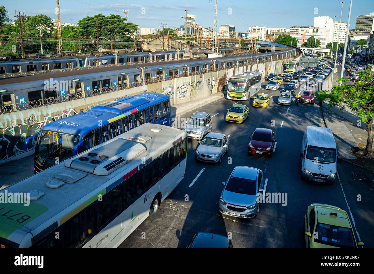 A Rio de Janeiro sono disponibili alcuni tipi di veicoli a noleggio e mezzi pubblici (da destra a sinistra): Taxi, furgone per pendolari, servizio autobus, treno su una parte elevata della linea 2 della metropolitana di Rio de Janeiro e treno suburbano sullo sfondo. Rei Pele avenue, quartiere di Sao Cristovao, zona nord della città. Foto Stock