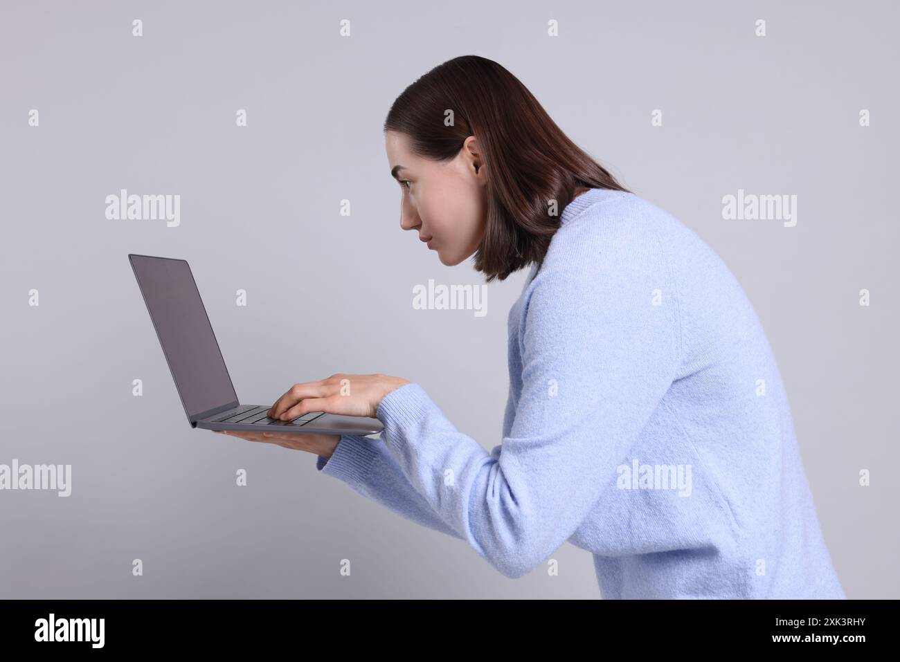 Donna con postura scarsa che utilizza un notebook su sfondo grigio Foto Stock