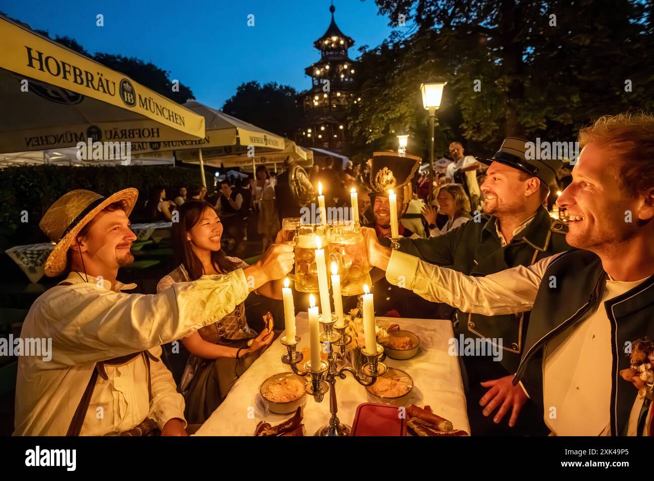 Kocherlball am Chinesischen Turm, Biertrinken bei Kerzenschein um 4:50 Uhr, München, 21. Juli 2024 Deutschland, München, 21. Juli 2024, Biertrinken bei Kerzenschein um 4:50 Uhr, Kocherlball am Chinesischen Turm, Englischer Garten, Freunde sind extra aus Wien gekommen, um hier mitzufeiern, Früh morgens, halb in der Nacht, trinken ein Bier, essen eine Brotzeit, tragen Tracht, Tradition entstand im 19. Jahrhundert, als Hauspersonal, Dienstboten und KöchInnen in den frühen Morgenstunden vor Dienstbeginn gefeiert und getanzt haben, Tradition wurde ab 1989 wiederbelebt, traditionell am 3. Sonntag im Foto Stock