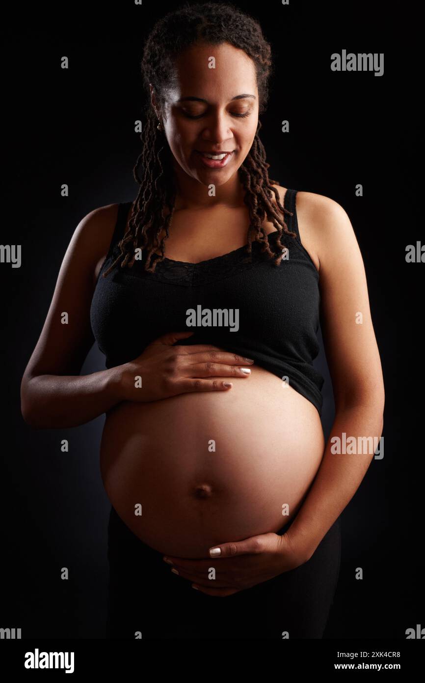Incinta, donna e sorriso con stomaco in studio, scossa del bambino e madre in attesa felice per la gravidanza. Sfondo nero, periodo di gestazione e. Foto Stock