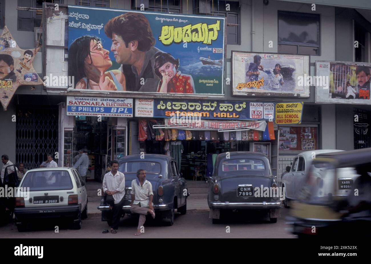 Persone e auto di fronte ai poster dei film nella città di Mysore, nella provincia di Karnataka in India. India, Mysore, marzo 1998 Foto Stock