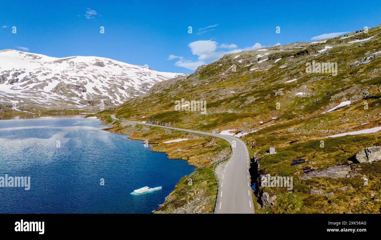 Una strada panoramica si snoda attraverso un paesaggio montuoso in Norvegia. La strada abbraccia il bordo di un lago blu scintillante, con montagne innevate sullo sfondo. Strynefjellsvegen, Geiranger, Norvegia Foto Stock