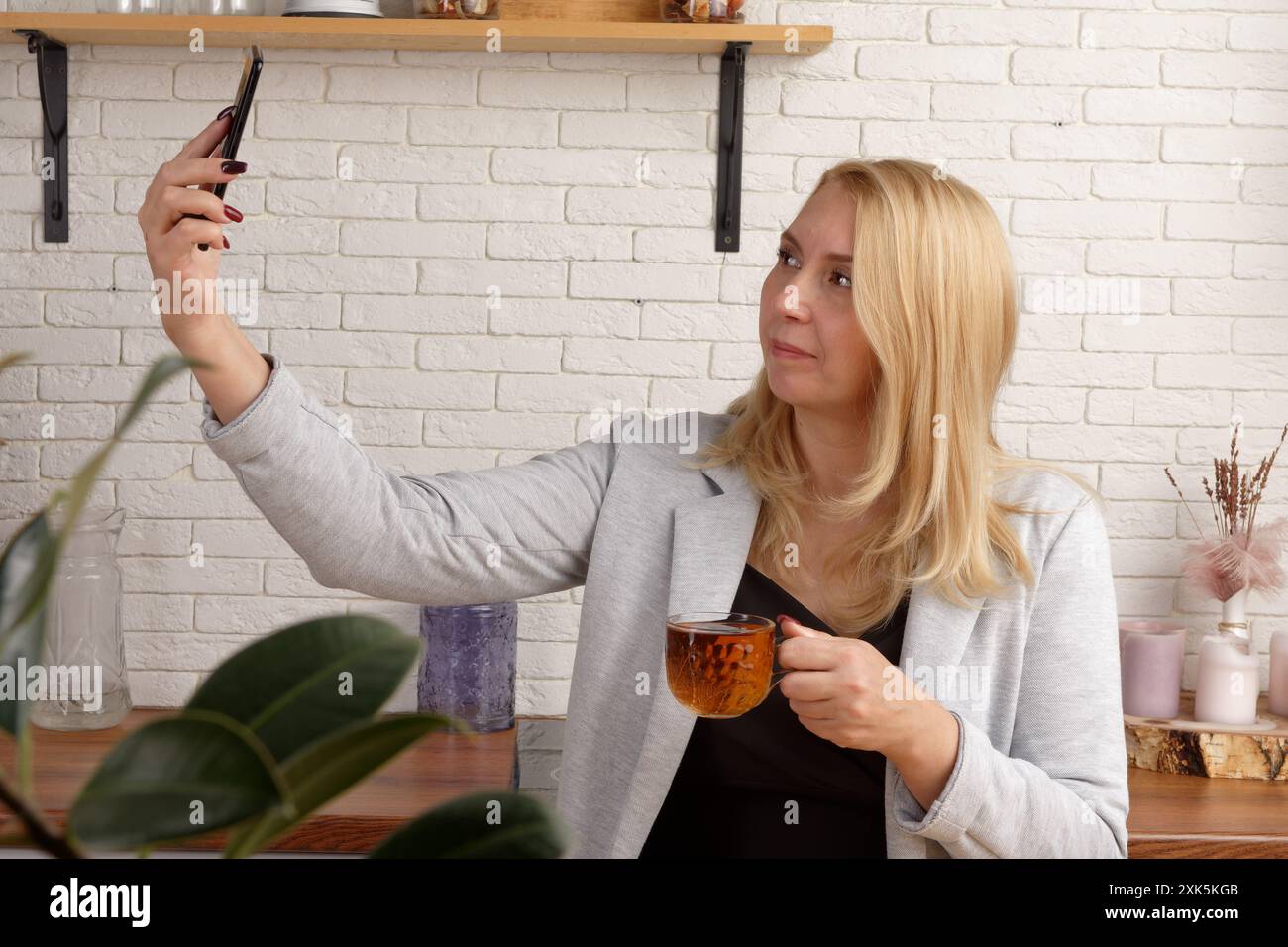 Senior professionista contemplativa che si gode un momento di relax durante la sua intensa giornata di lavoro, tenendo una tazza di tè in una mano e uno smartphone nella Foto Stock