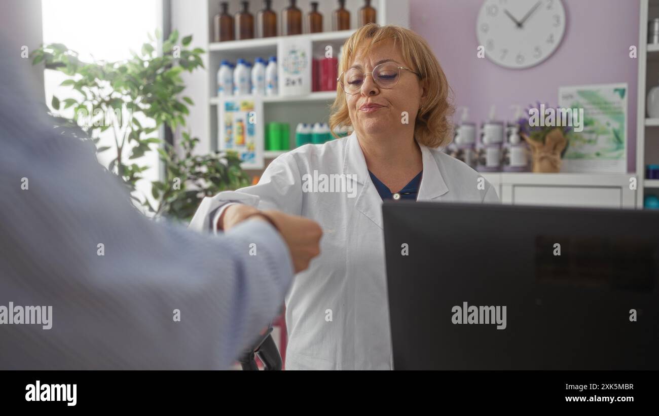 Farmacista anziana che assiste un cliente all'interno di una farmacia con scaffali di prodotti e un orologio a parete. Foto Stock