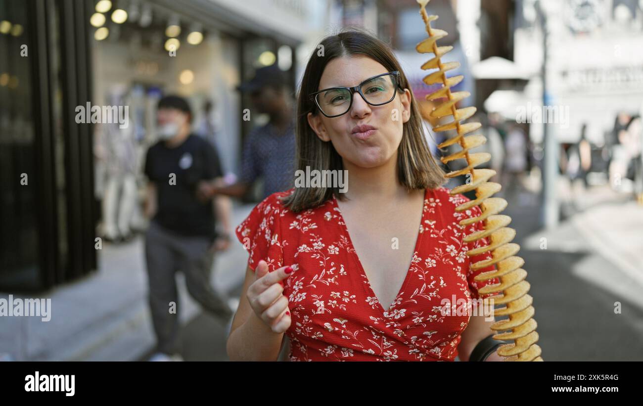 Bella donna ispanica che mangia deliziosamente patatine croccanti e deliziose su un bastone in takeshita Street, tokyo - amante del cibo spazzatura viaggiante, occhiali sportivi Foto Stock