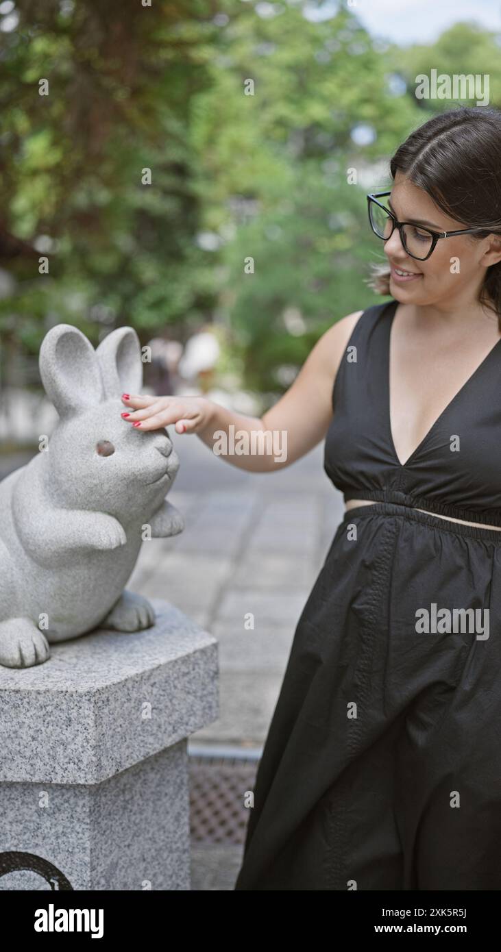 Felice ritratto di una bella donna ispanica in occhiali, in piedi allegramente accanto a una graziosa statua di coniglio nell'antico tempio jinja di okazaki, incarnato Foto Stock