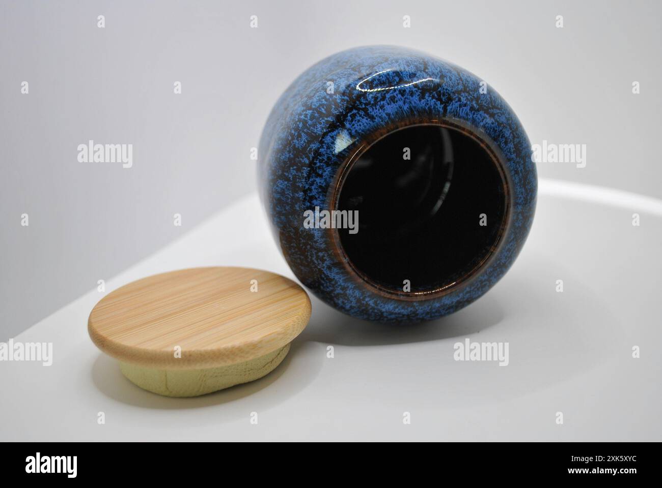 Vaso in ceramica blu e marrone con coperchio in legno su superficie bianca Foto Stock