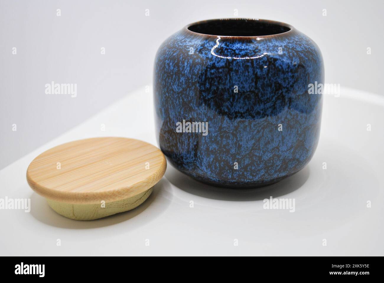 Vaso in ceramica blu e marrone con coperchio in legno su superficie bianca Foto Stock
