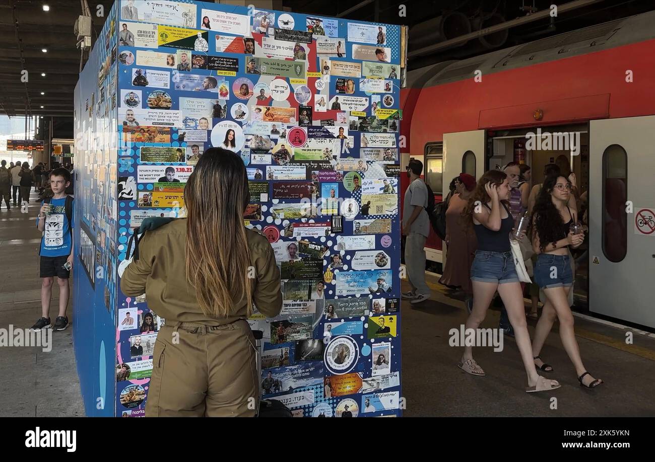 TEL AVIV, ISRAELE - 21 LUGLIO: una donna soldato israeliana si trova accanto a un muro con adesivi commemorativi che commemorano i soldati IDF uccisi nella guerra israeliana a Gaza e ter­ror vic­tims dopo Octo­ber 7, nella stazione ferroviaria hashalom, in mezzo alle continue battaglie tra Israele e il gruppo militante Hamas a Gaza il 21 luglio 2024 a Tel Aviv. Israele. Foto Stock