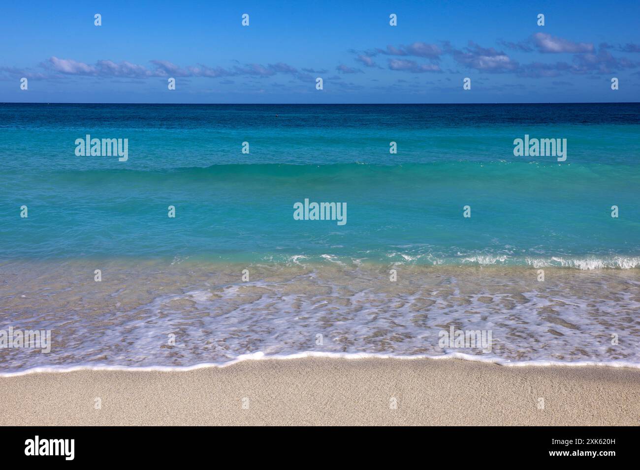 Spiaggia di mare vuota con sabbia bianca, vista delle onde azzurre e del cielo blu con nuvole. Costa caraibica, sfondo per vacanze in una natura paradisiaca Foto Stock